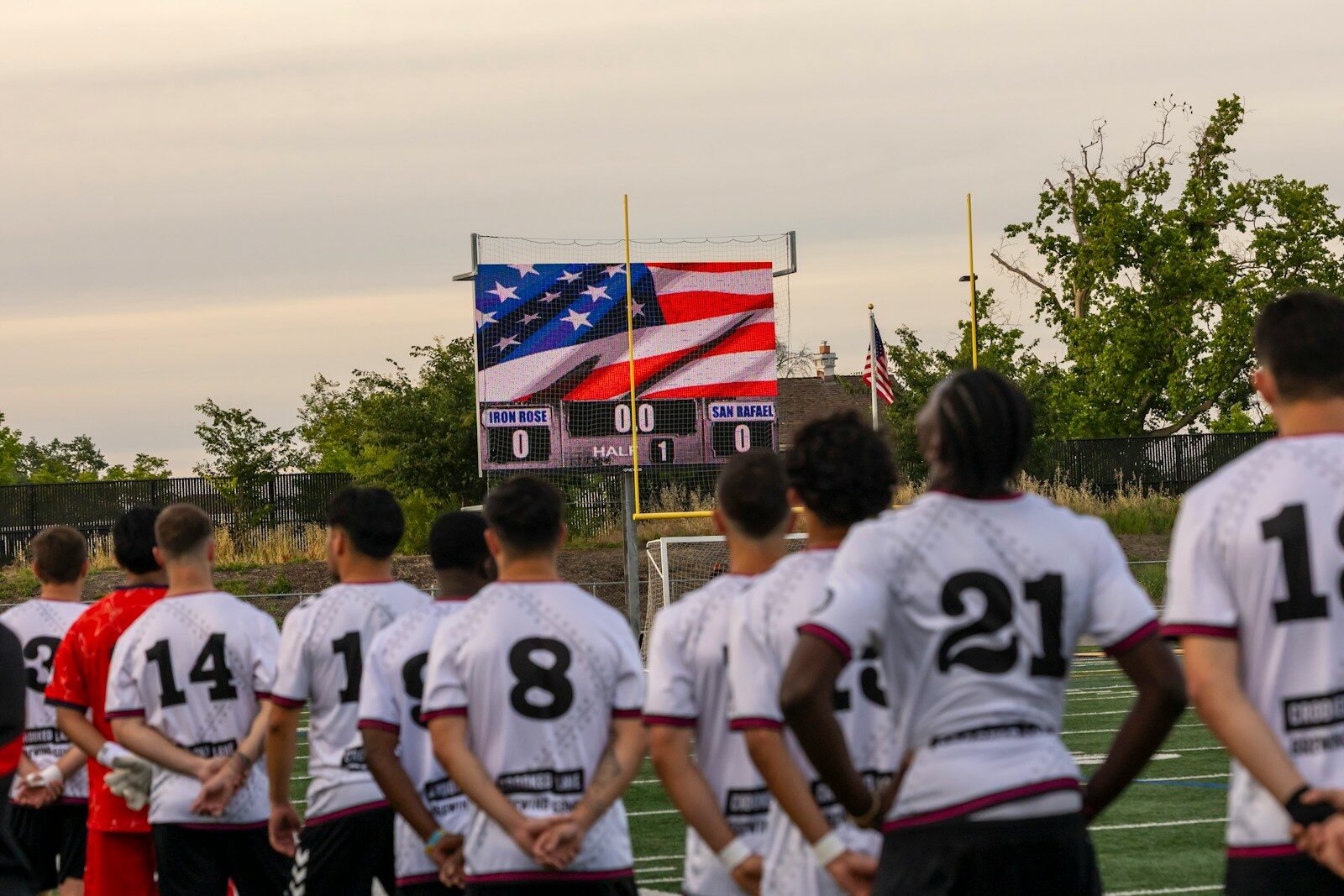 Soccer players stand facing a scoreboard with american flag.